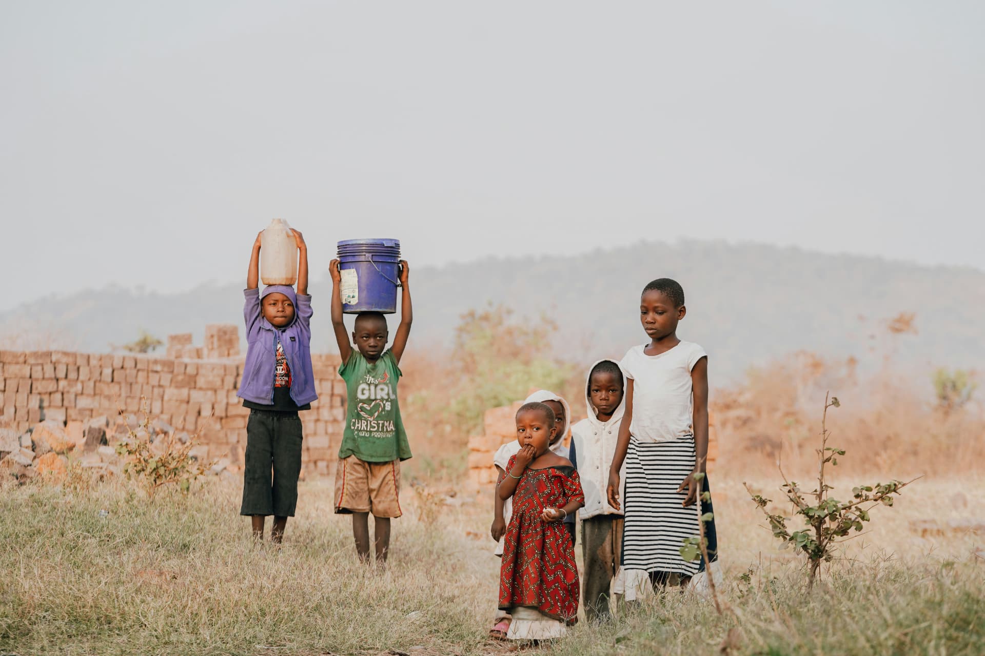 Children carrying water containers across dry land